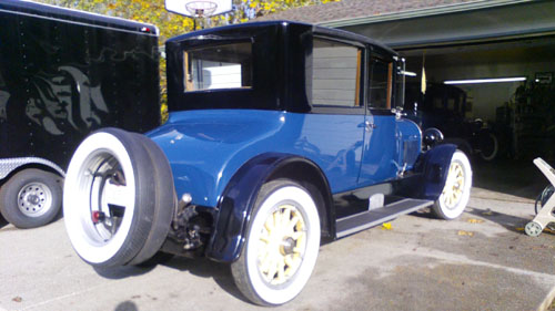 Rear view of a 1923 Cadillac coupe outside a garage. 