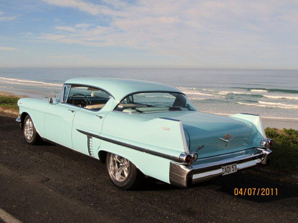 view of a 1957 cadillac from the rear with a beach in the background.