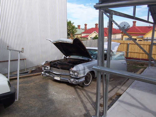 1959 Cadillac outside a garage with the hood up.